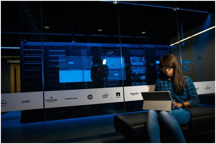 Woman using a laptop in a server room, showcasing