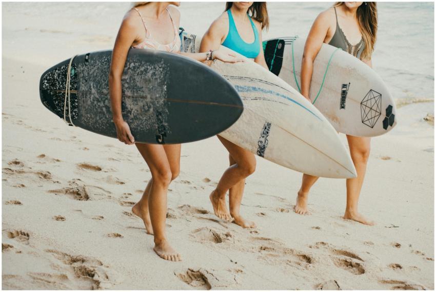 Three women carrying surfboards along a sandy Bali
