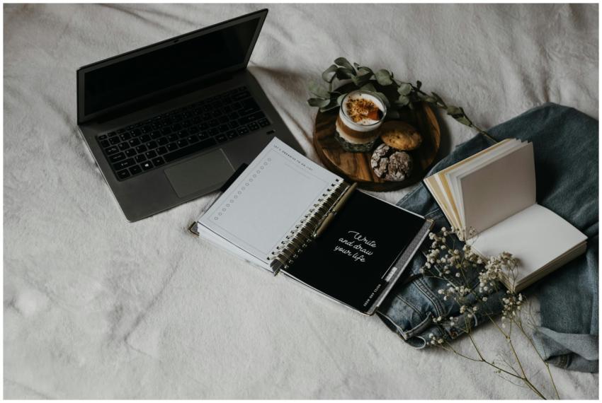 A cozy flat lay of a laptop, journals, and snacks