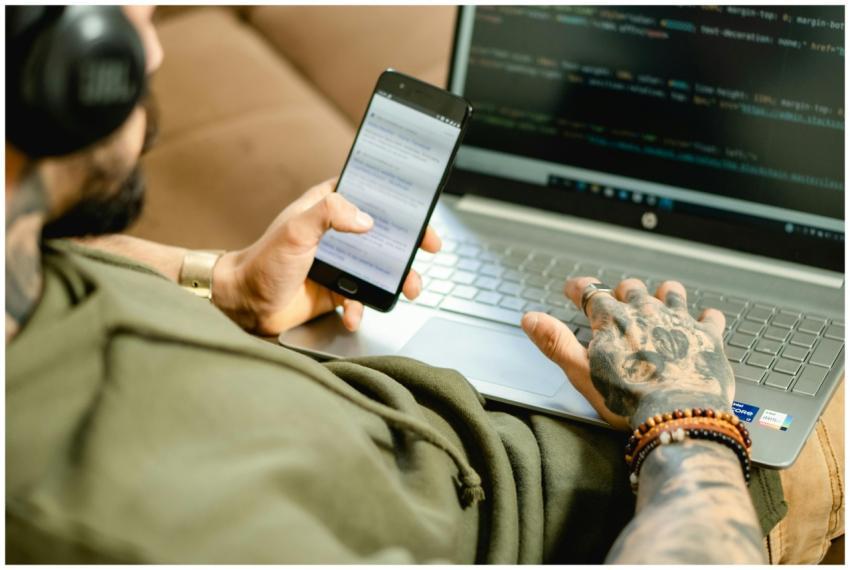 A tattooed person engaged in coding on a laptop wh