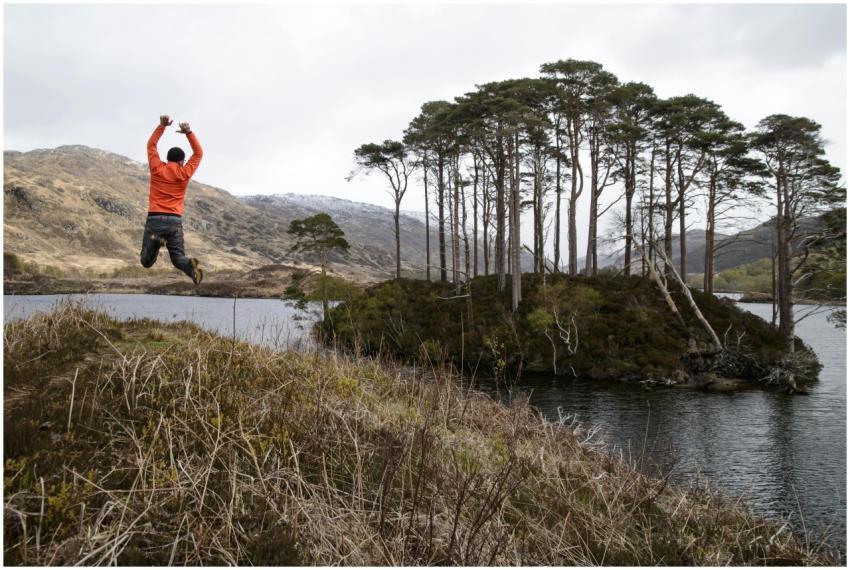 Man jumps joyfully by a scenic lake in the Highlan