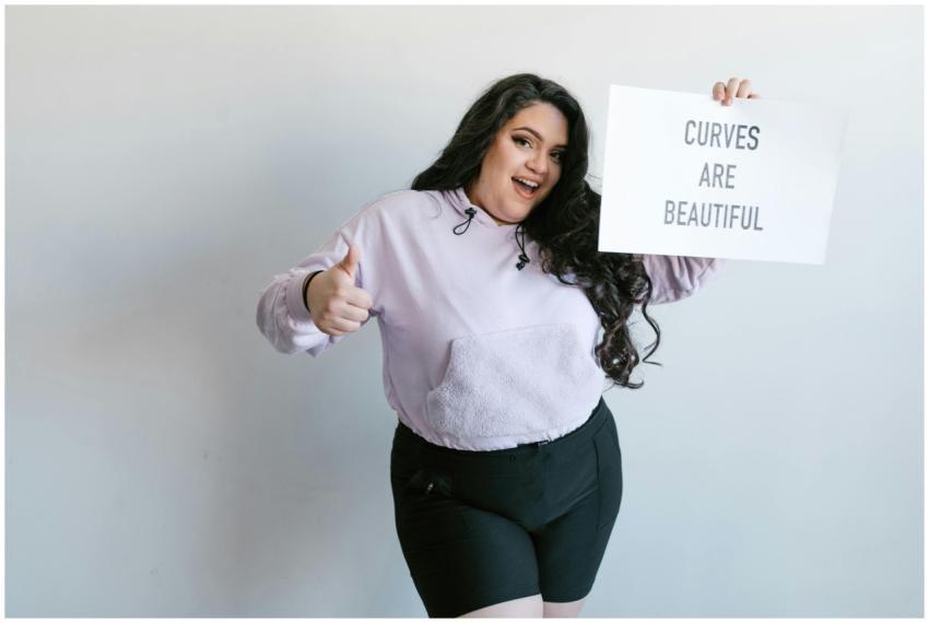 Cheerful plus-size woman holding sign 'Curves Are