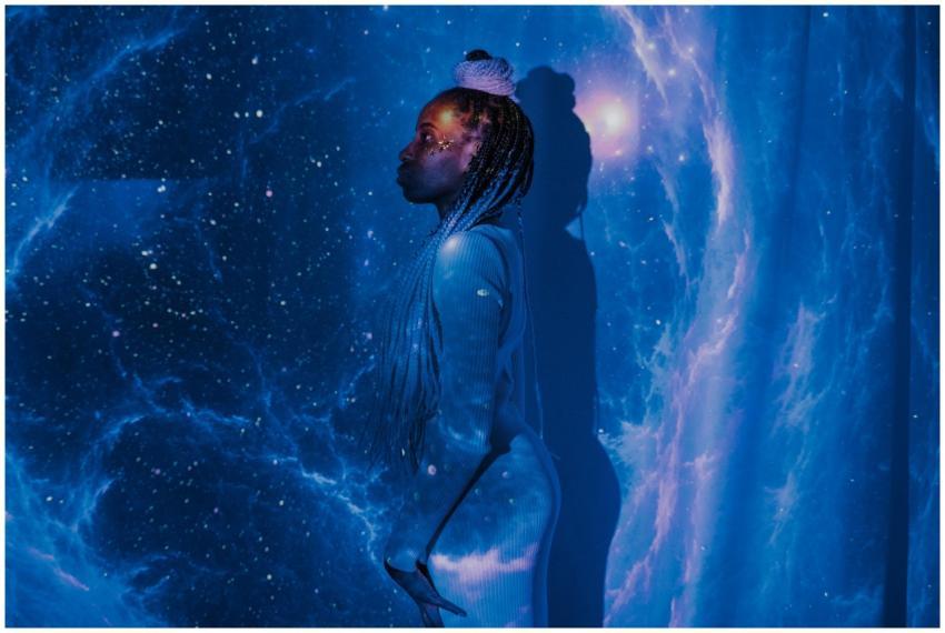 A woman stands against a galaxy projection with a