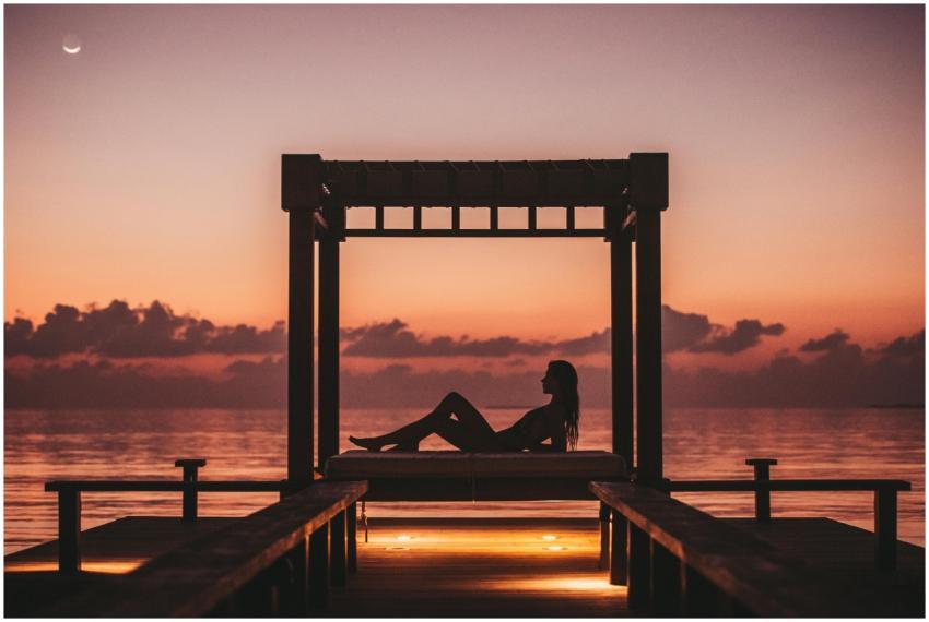 A woman relaxes on a dock at sunset in the Maldive