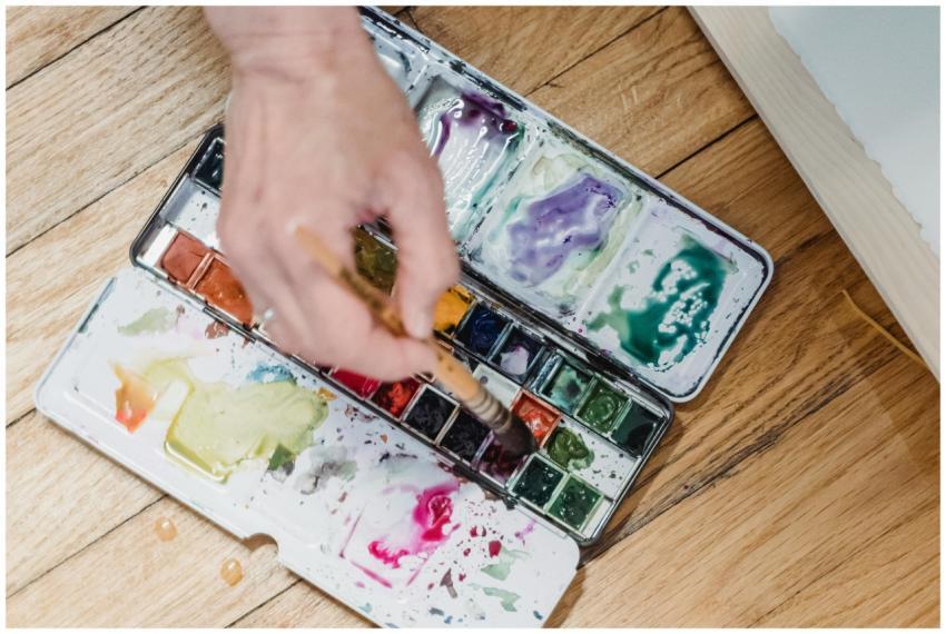 Close-up of a hand using a watercolor palette with