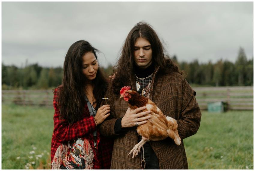 A bohemian couple standing outdoors with a chicken