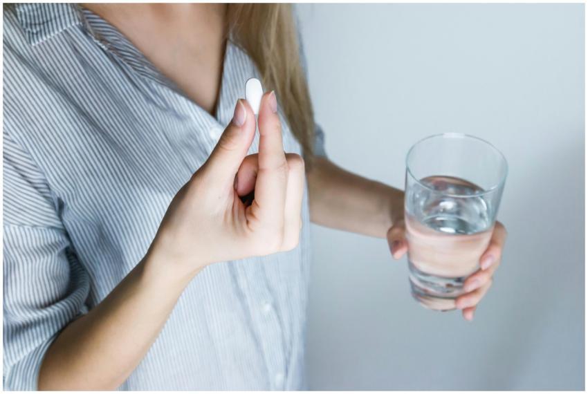 Close-up of a woman holding a pill and a glass of