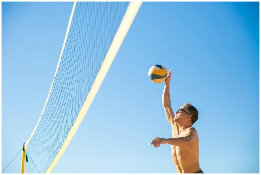 An athletic man jumps to hit a volleyball over the
