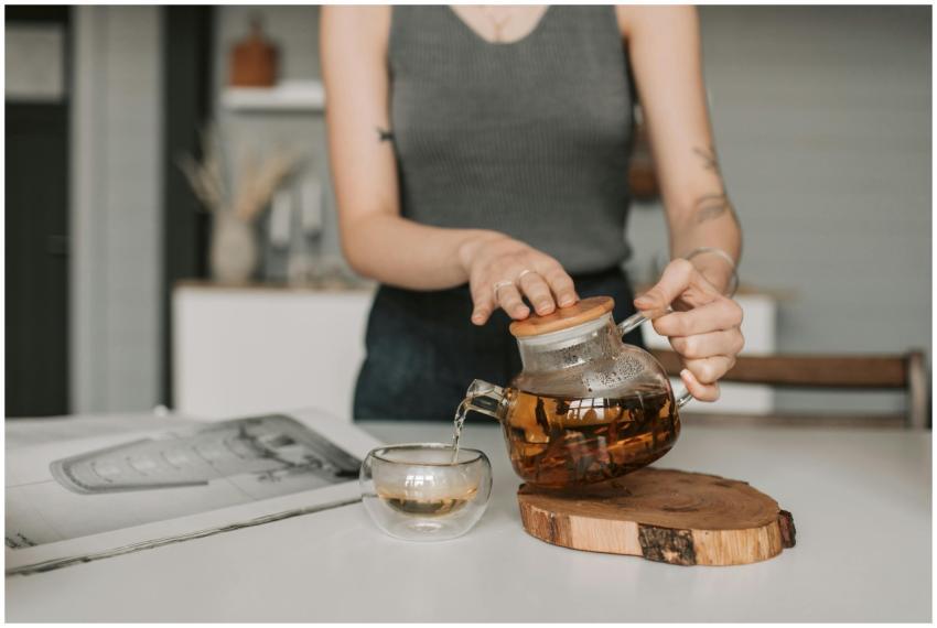 A woman pours herbal tea from a clear glass teapot