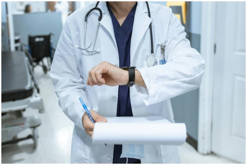 Doctor in lab coat checking wristwatch while holdi