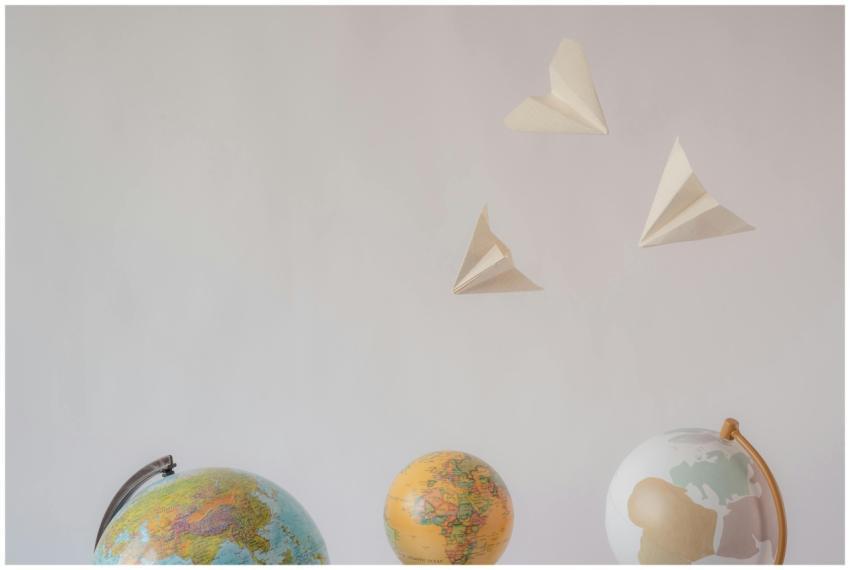 Paper airplanes fly over colorful globes, symboliz