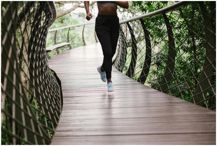 An athletic woman jogging on a nature trail bridge