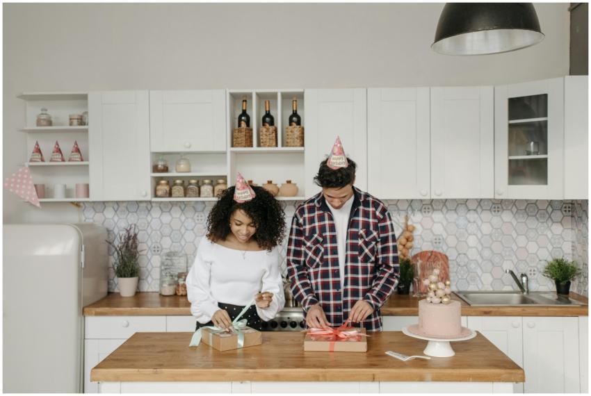 A couple in party hats wrap presents on a kitchen