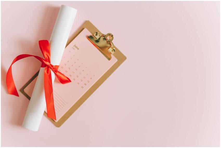 Rolled diploma with red ribbon on clipboard next t