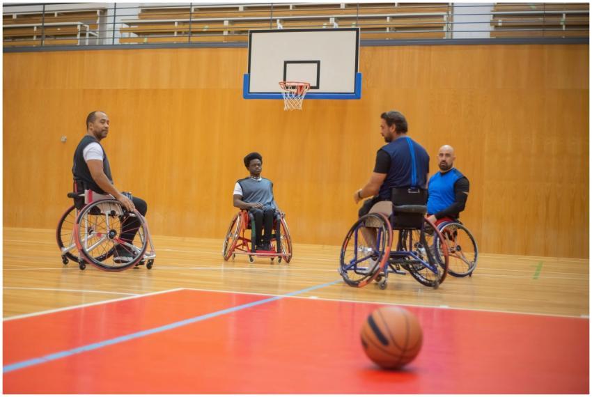 Four men in wheelchairs playing basketball indoors