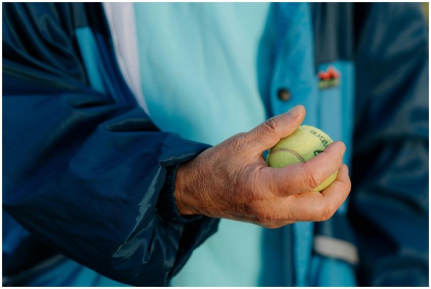 A close-up of a senior's hand holding a tennis bal