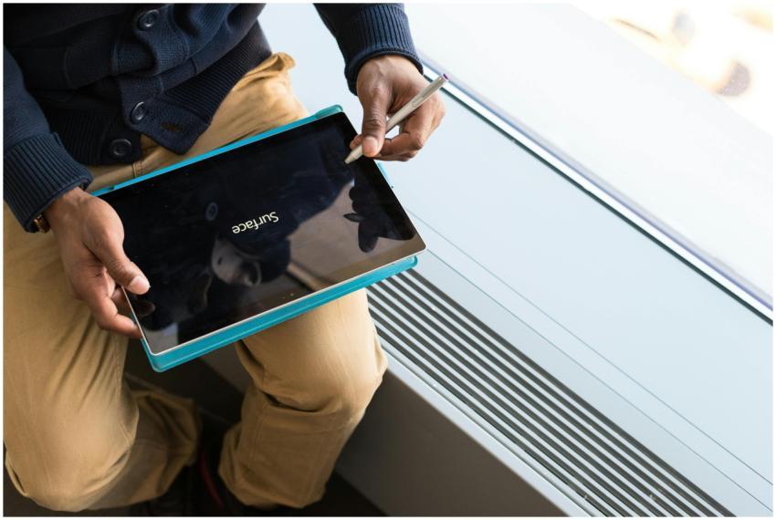 An adult seated by the window using a tablet devic