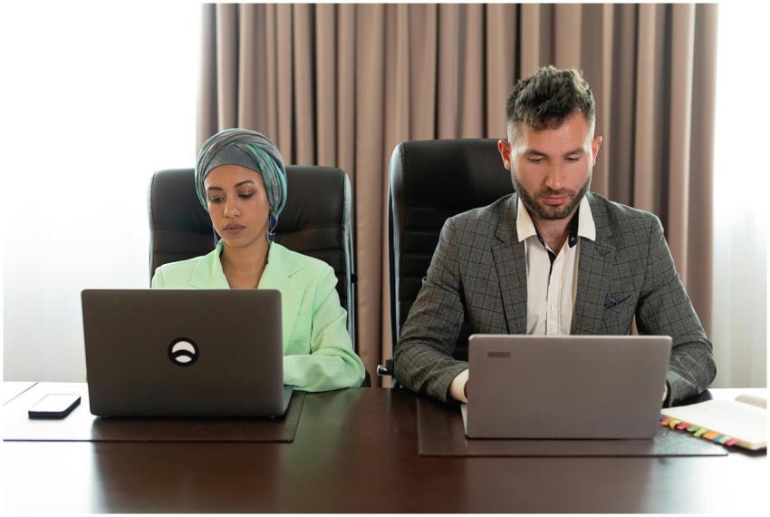 Two professionals working together on laptops in a