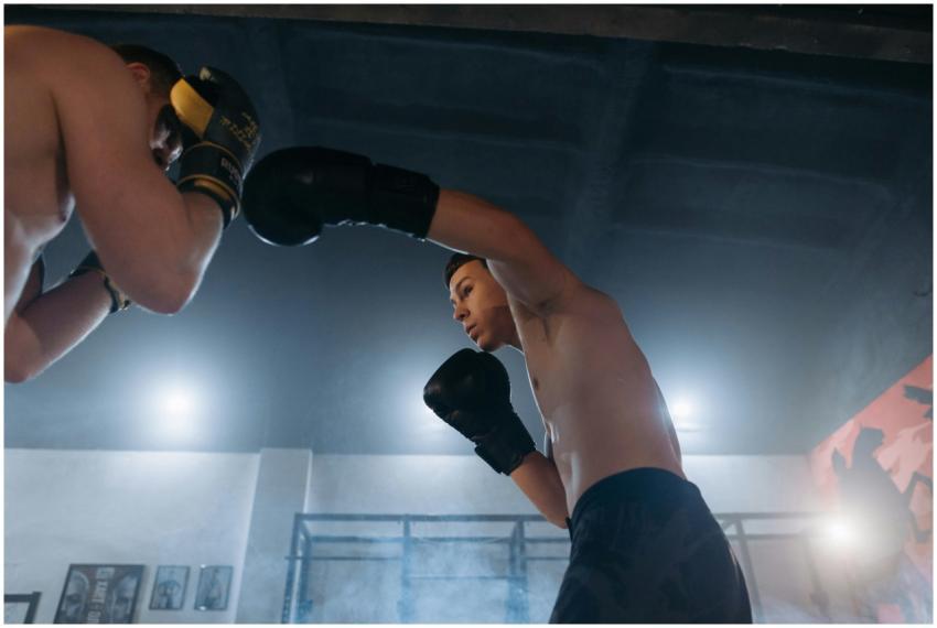 Two shirtless boxers sparring intensely in a gym,
