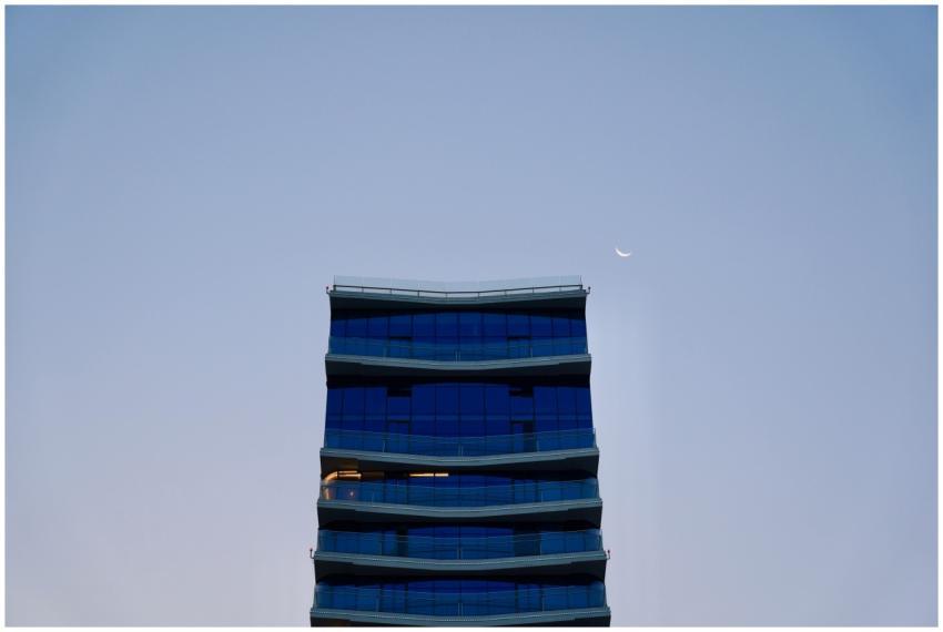 Curved blue glass building against sky with cresce