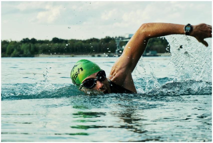 A male swimmer in a green cap and goggles competin