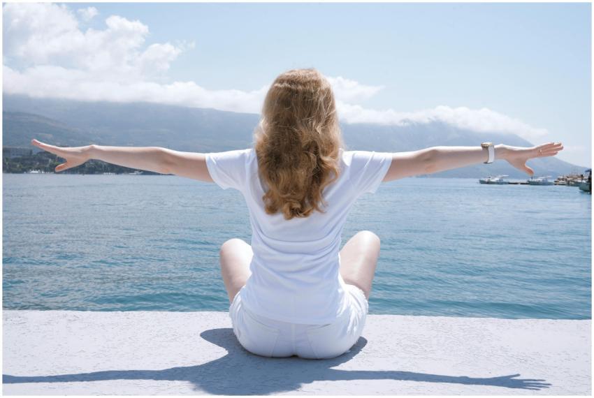 Woman sitting with open arms by the water, embraci