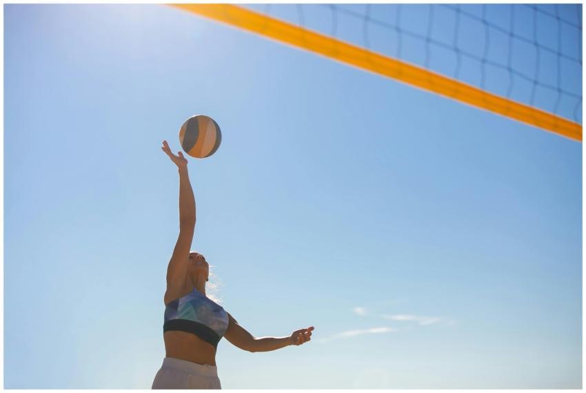 A woman spiking a volleyball on a sunny beach with