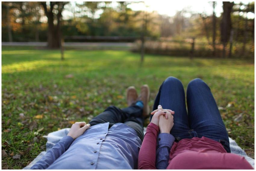 A romantic couple holds hands while lying on grass