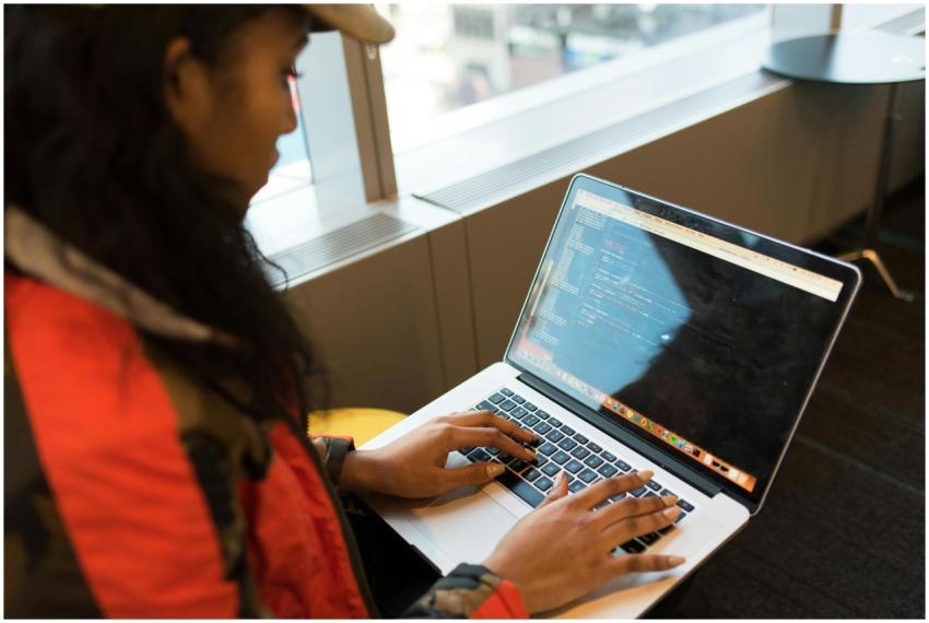 A focused woman typing code on her laptop indoors,
