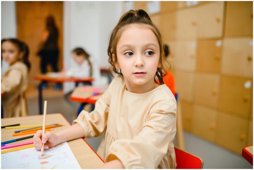 A young girl sitting at a desk coloring with crayo