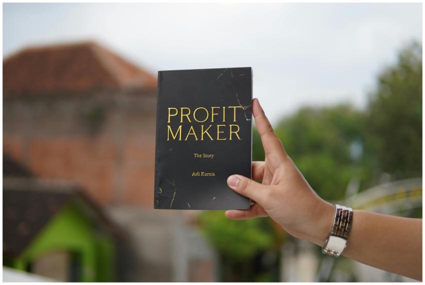 Close-up of a hand holding the book 'Profit Maker'