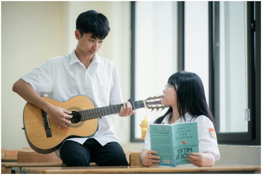 Two teenagers in a classroom: one playing guitar,