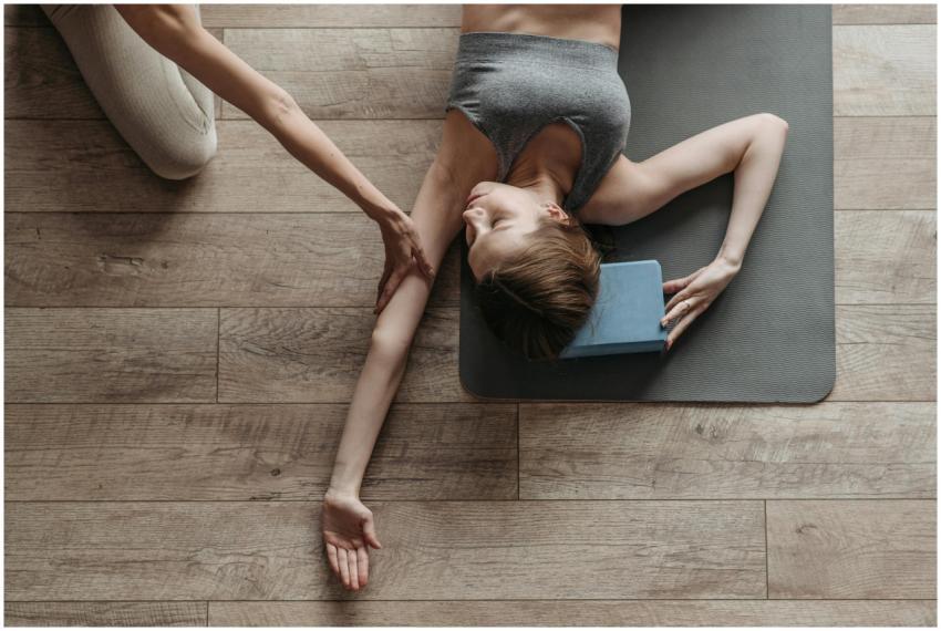 Woman lying on yoga mat being assisted in stretchi