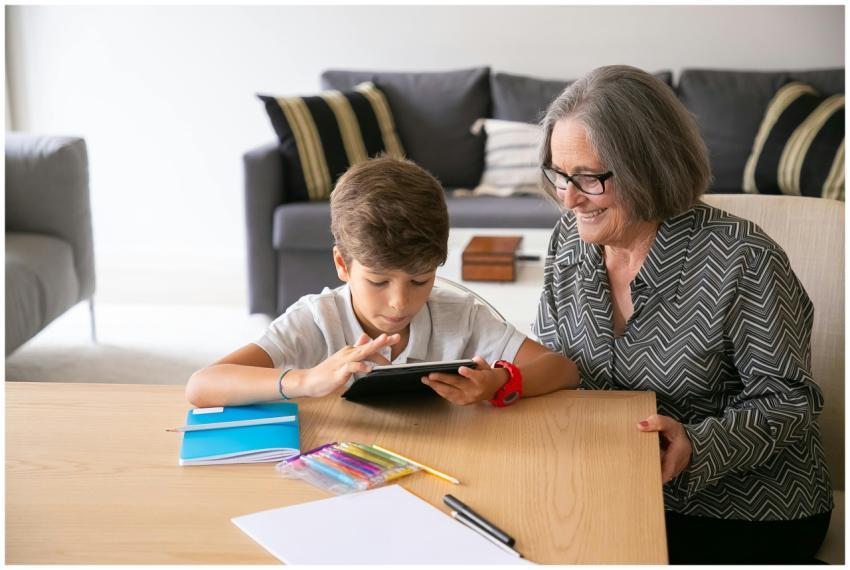 A senior woman smiles while helping her grandson w