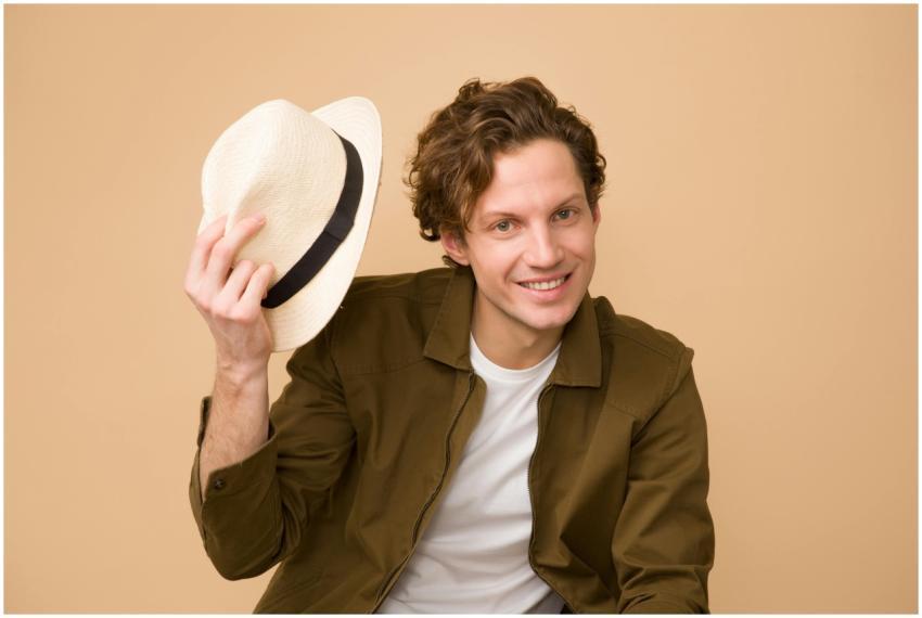 A cheerful man with curly hair tips his hat in a b