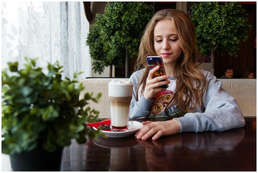 A young woman enjoys a latte while browsing her sm