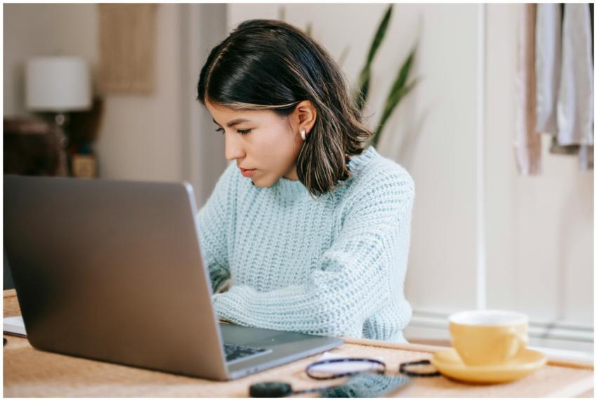 Focused young woman using laptop at home while dri