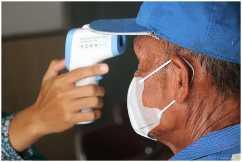A senior man wearing a mask gets his temperature c