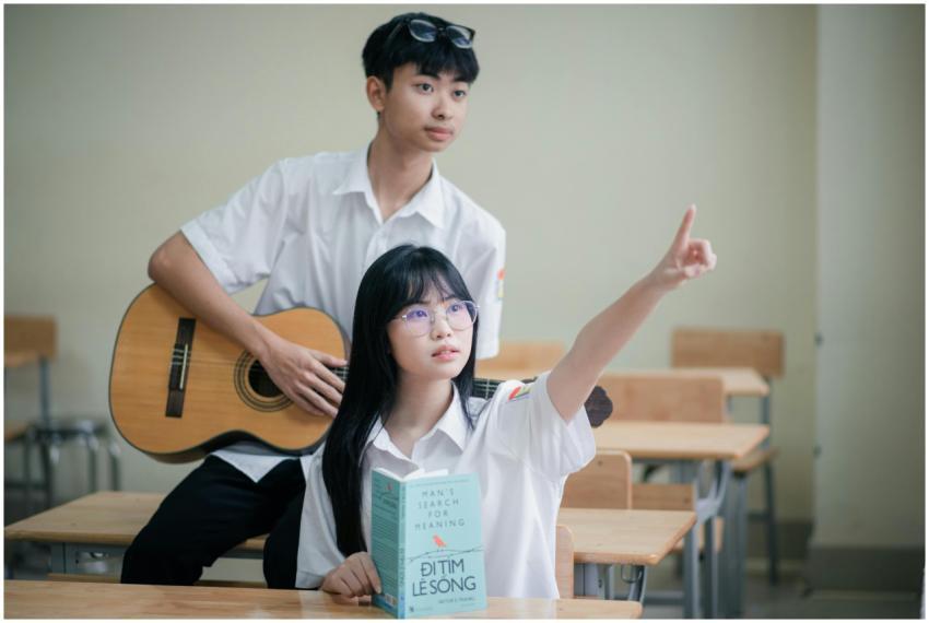 Two teenagers in a classroom, one playing guitar,