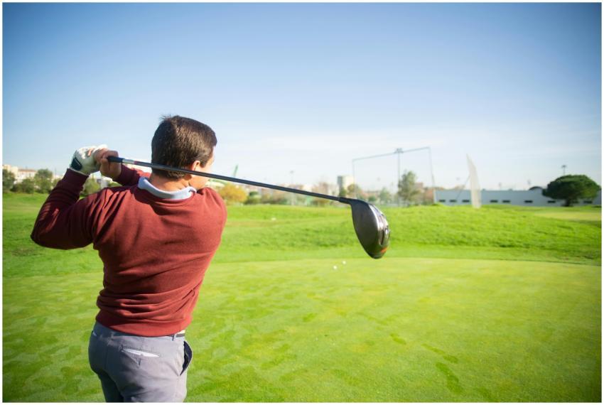 A golfer in a red sweater swings on a sunny day in