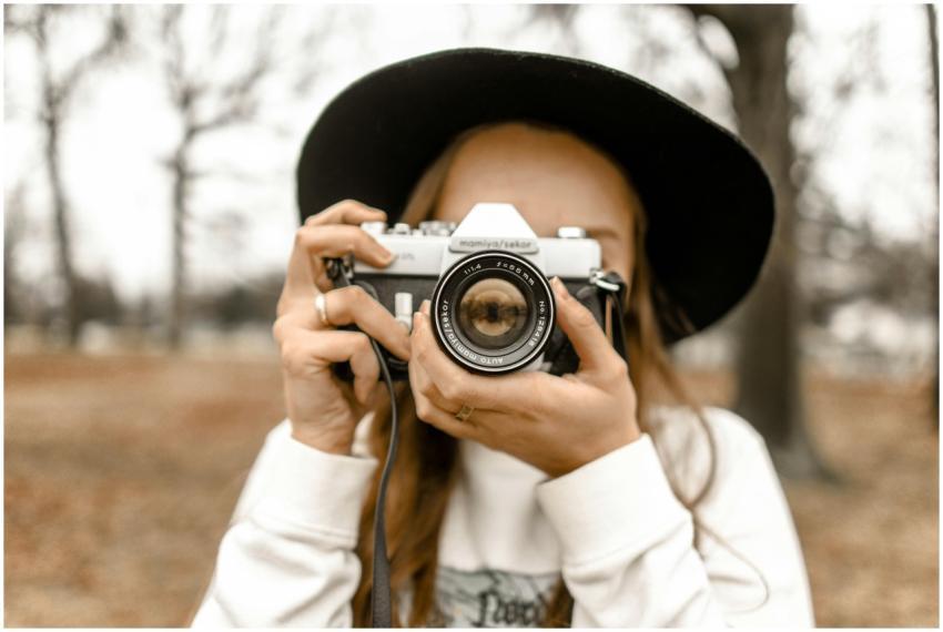 Stylish woman in black hat holding a vintage camer