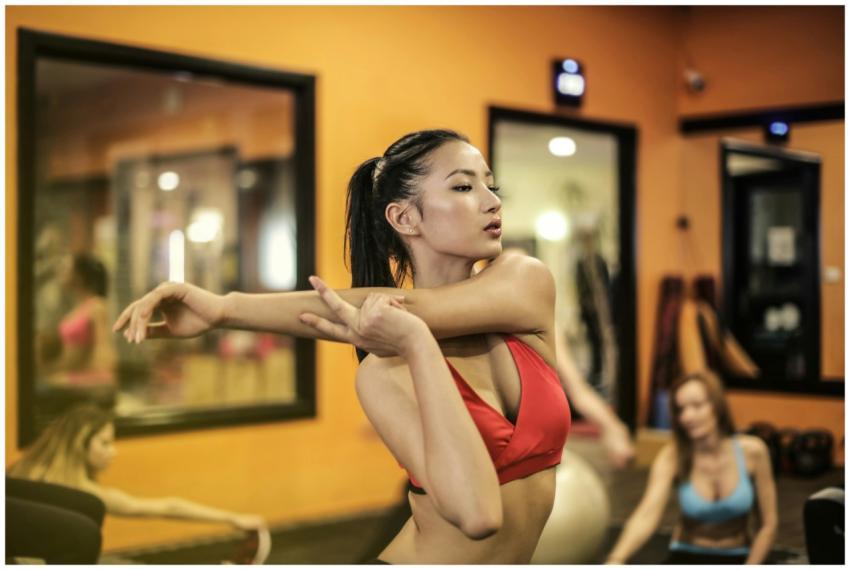 Young woman exercising in a gym, stretching arm mu