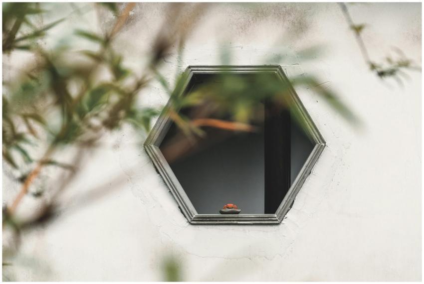 A hexagonal window on a white wall with blurred br