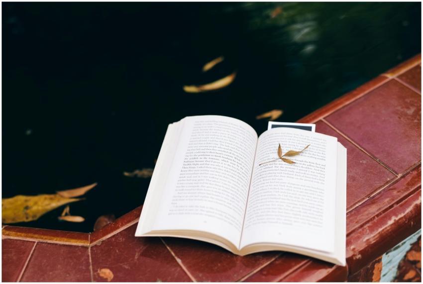 An open book with a leaf on a poolside, capturing