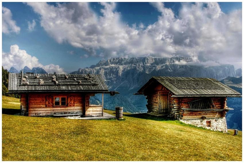 Two rustic cabins on a grassy hillside with dramat