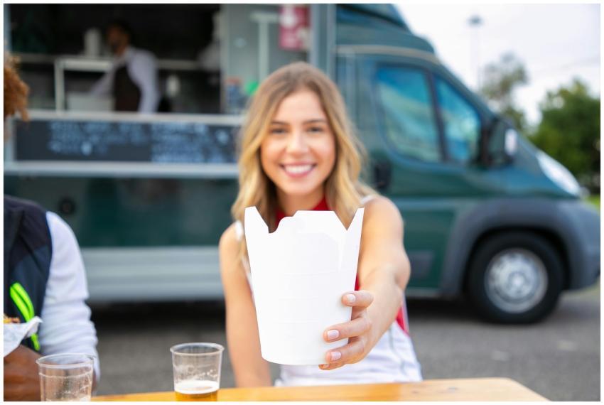Smiling woman offers takeaway box in front of a fo