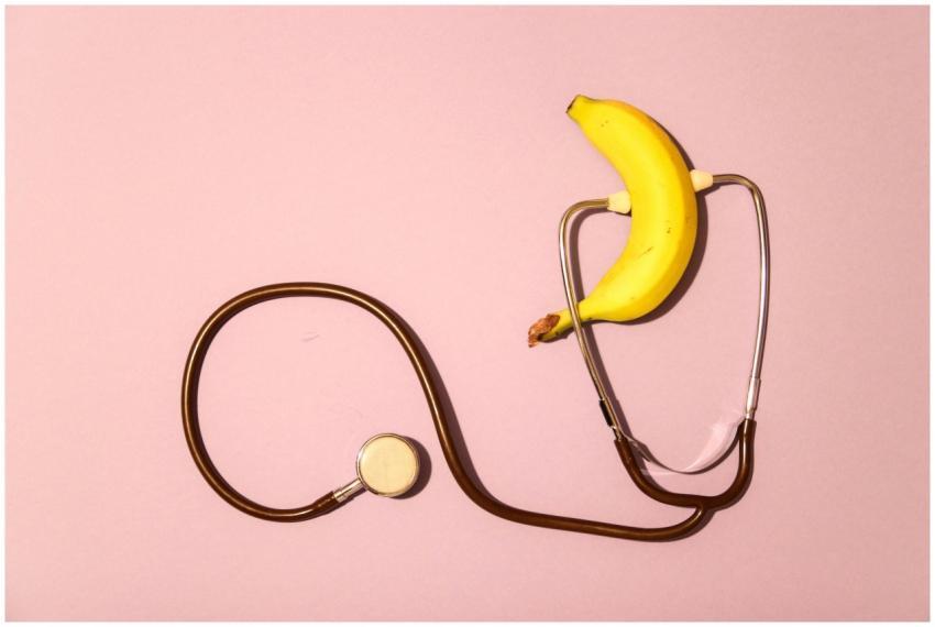 A banana wrapped in a stethoscope on a pink surfac