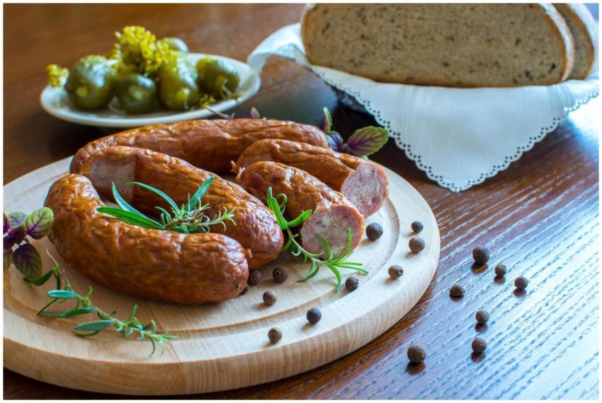Appetizing smoked sausages on wooden platter with
