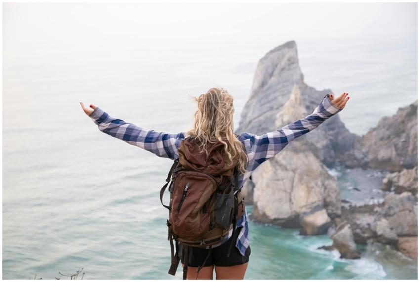 Woman with backpack stands on mountainside with ar