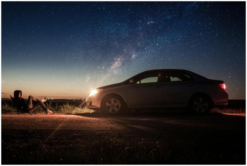 A person relaxes by their car under a starry night
